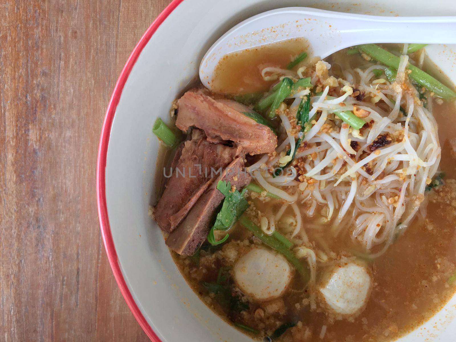 Delicious noodles with pork and pork balls with soup in white in Thai style food. Thai peoples call Boat Noodles, breakfast with bowl on wooden background meat. Noodle of traditional Thai food.