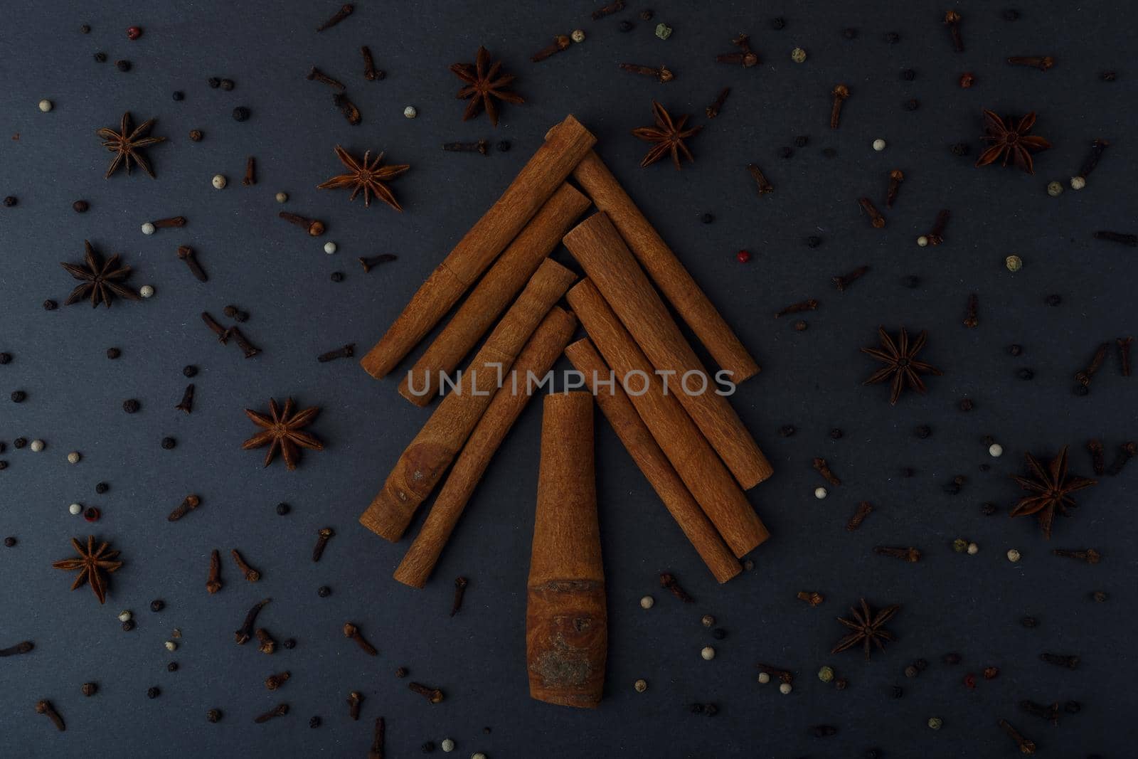 Flat lay with christmas tree made of cinnamon sticks on dark black table decorated with with spices. Winter holidays and cooking concept. High quality photo