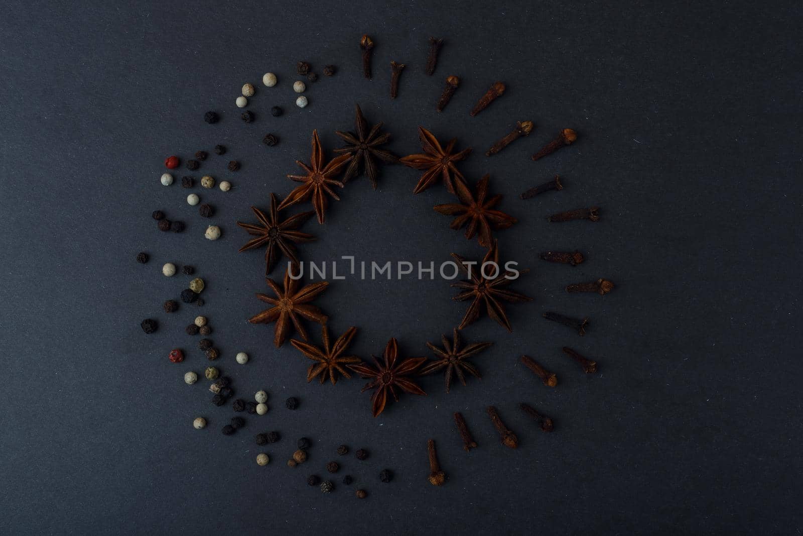 Top view of two circles made of different spices, anise stars, pepper and dry cloves on dark black table. Concept of cooking and baking with spices. 