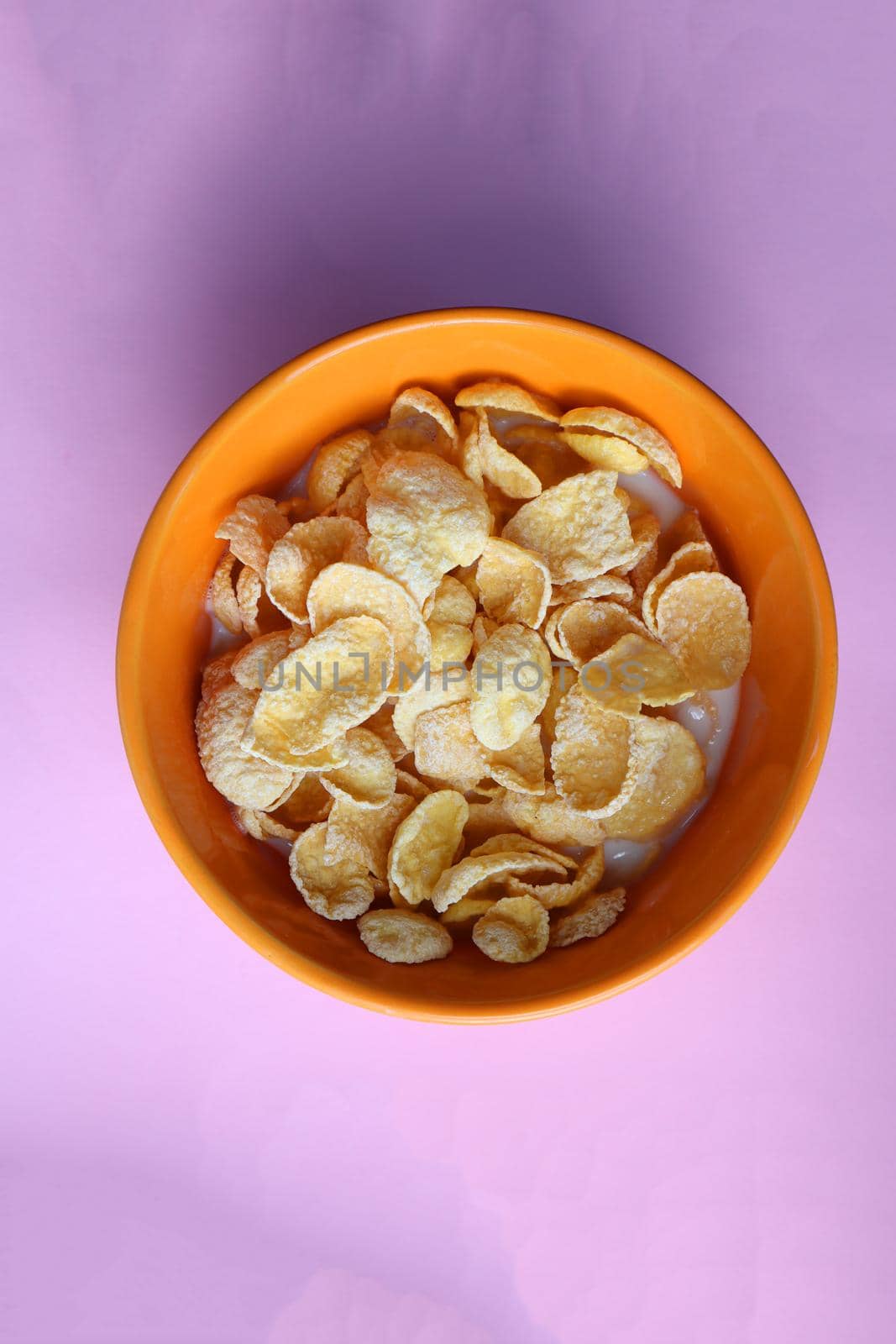 Cornflakes  in an orange plate. Orange plate on a pink background