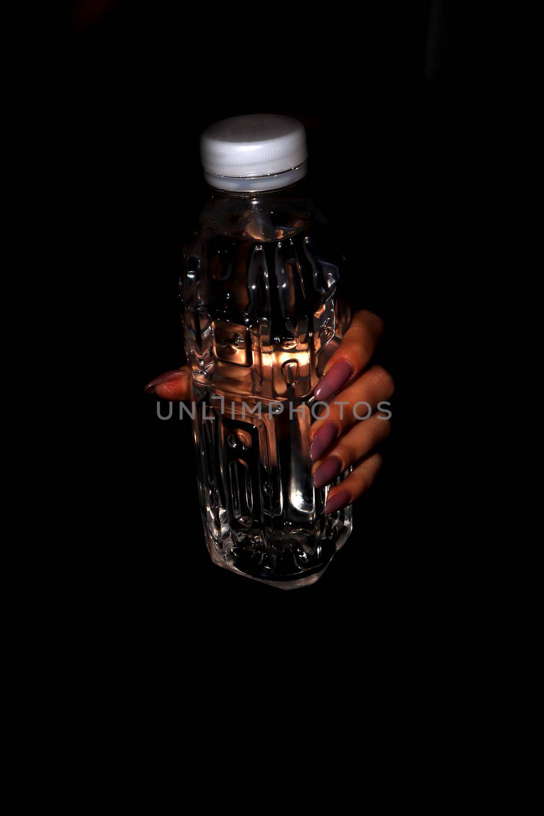 Transparent plastic bottle of water without a label in a woman's hand with long nails.