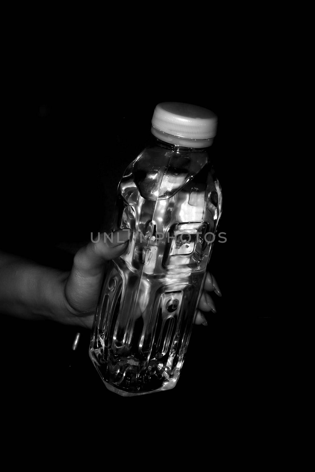 Transparent plastic bottle of water without a label in a woman's hand with long nails. Black and white photo