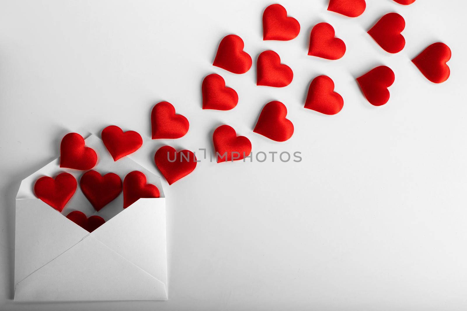 Valentine day love letter, envelope of white paper with red hearts heap spread on white background.