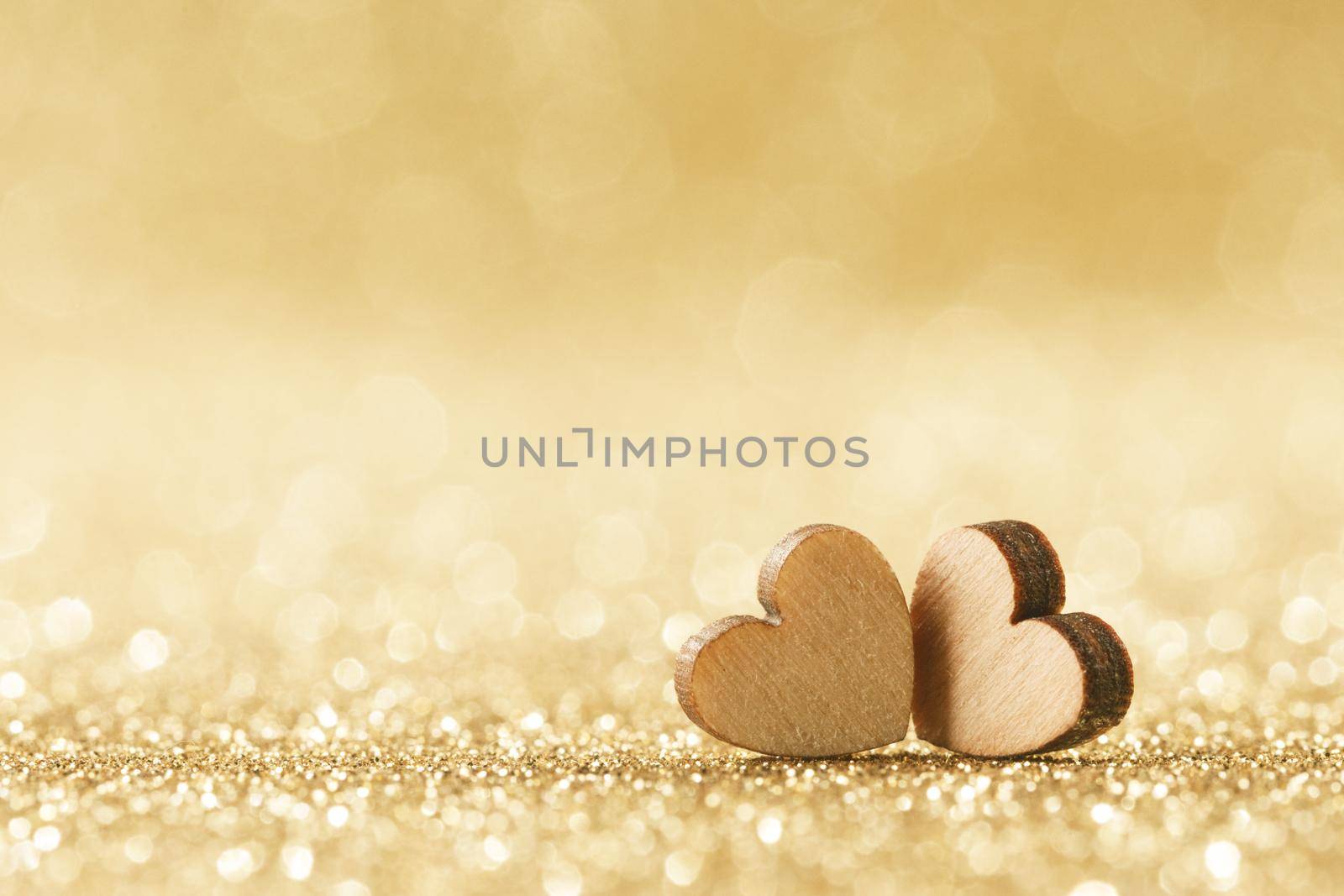 Two small handmade wooden hearts on bright golden lights bokeh background Valentines day card