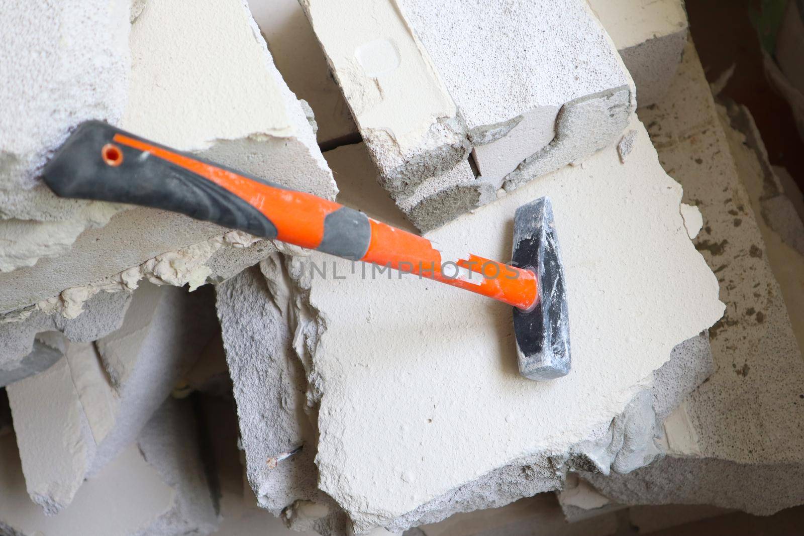 A hammer with a rubberized orange handle rests on a broken gas block