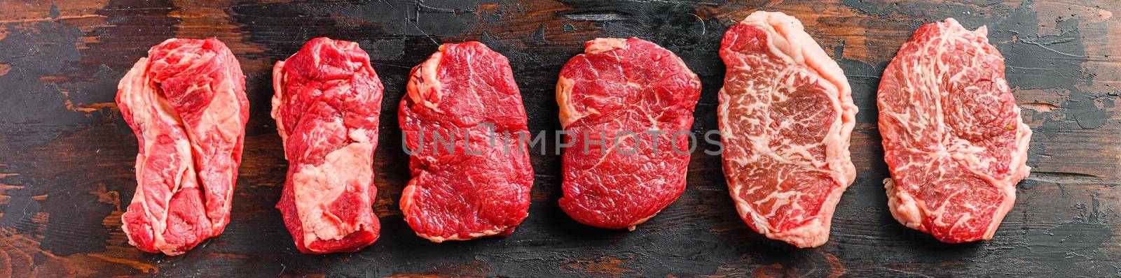 A set of different types of raw beef steaks:top blade, rump, chuck eye roll over old wooden background top view banner size. by Ilianesolenyi