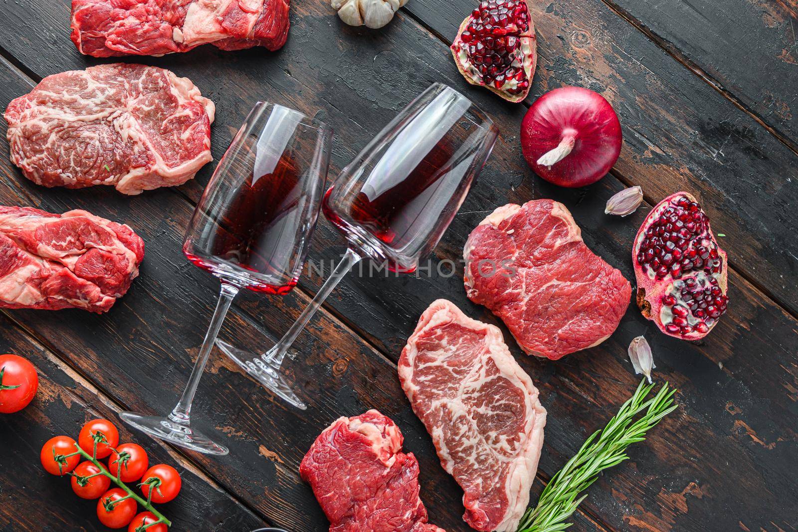 Meat beef steaks frame concept, with different steak cuts and two wine glasses in frame on dark old wooden table side view
