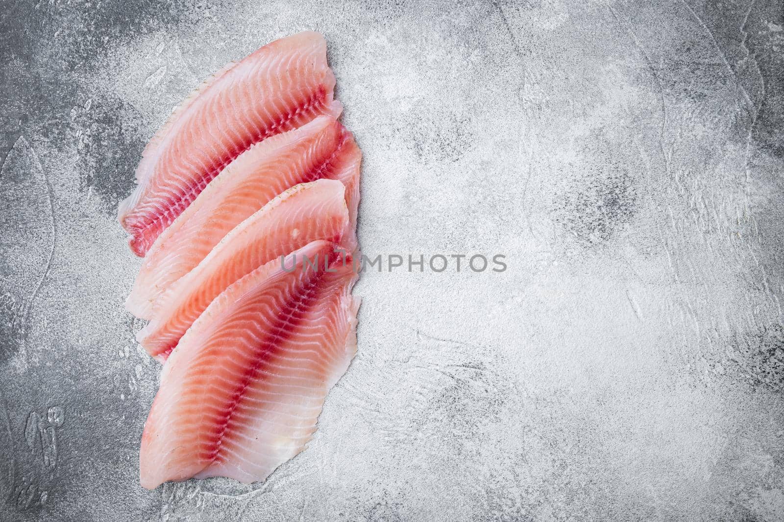 Tilapia fish, skinless meat, on gray background, top view with copy space for text