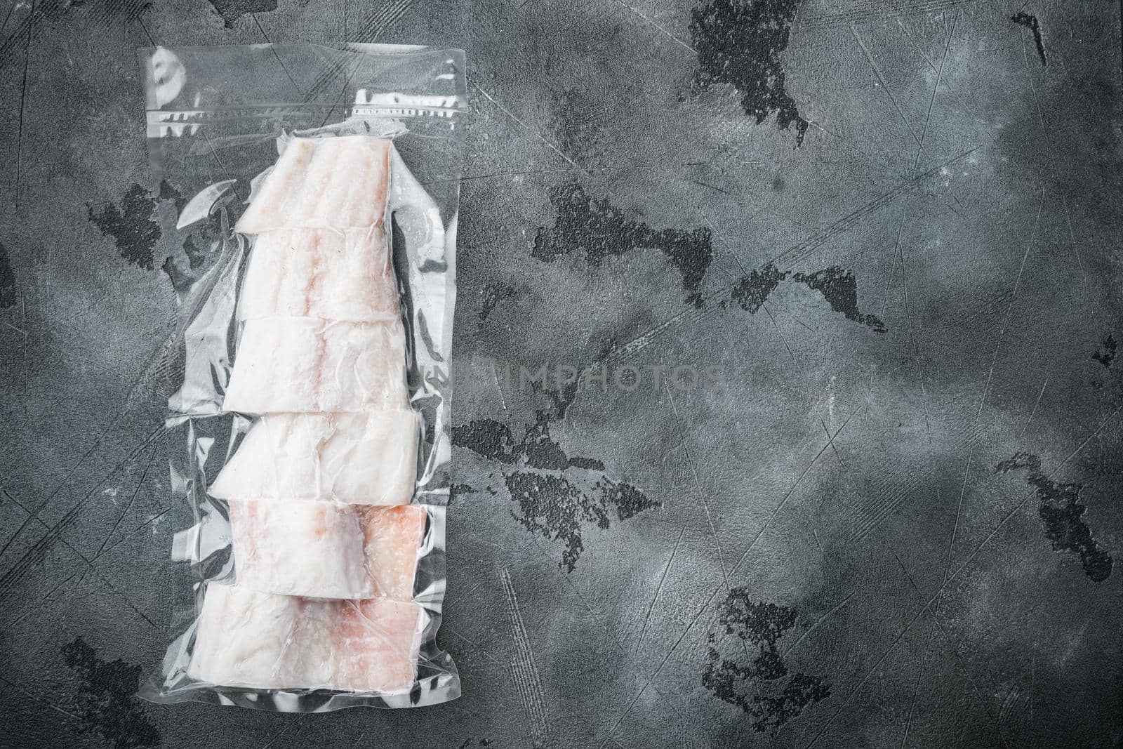 Raw haddock fish skinless plastic vacuum packaged, on gray background, top view with copy space for text