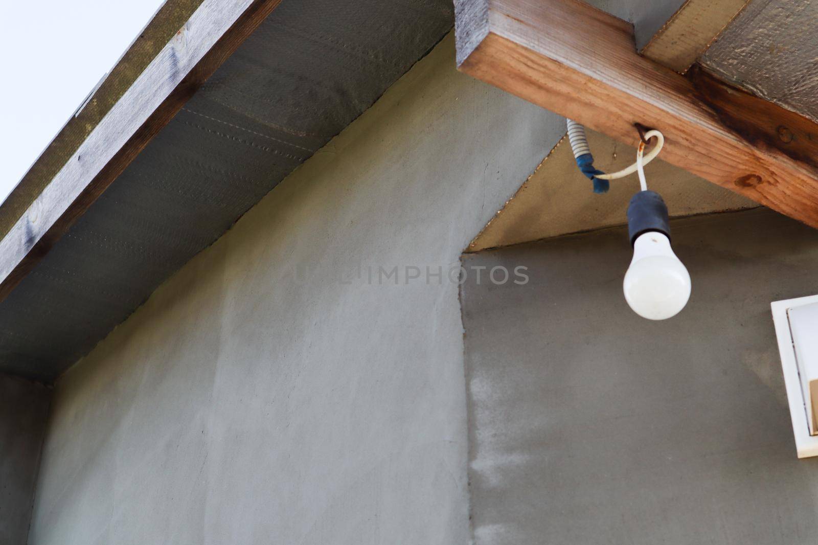 On the porch hangs a white light bulb on a wooden beam