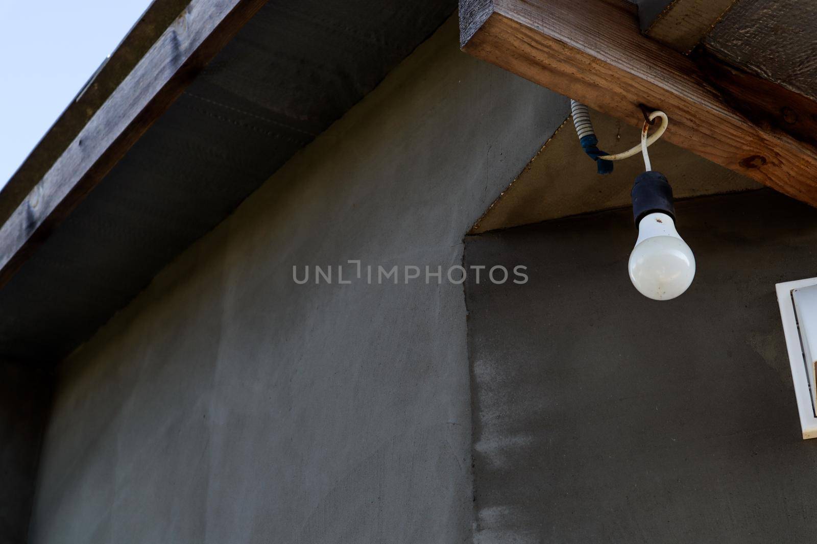 On the porch hangs a white light bulb on a wooden beam