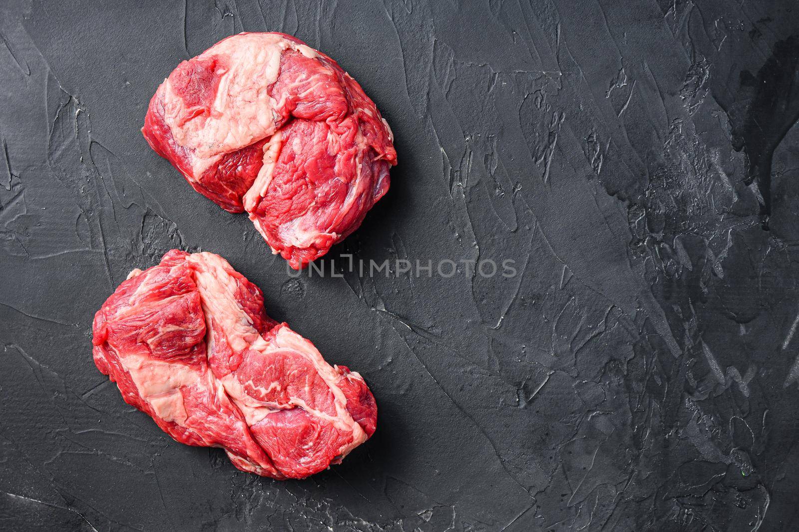 Organic chuck eye roll steak cuts, top view on black textured table with space for text
