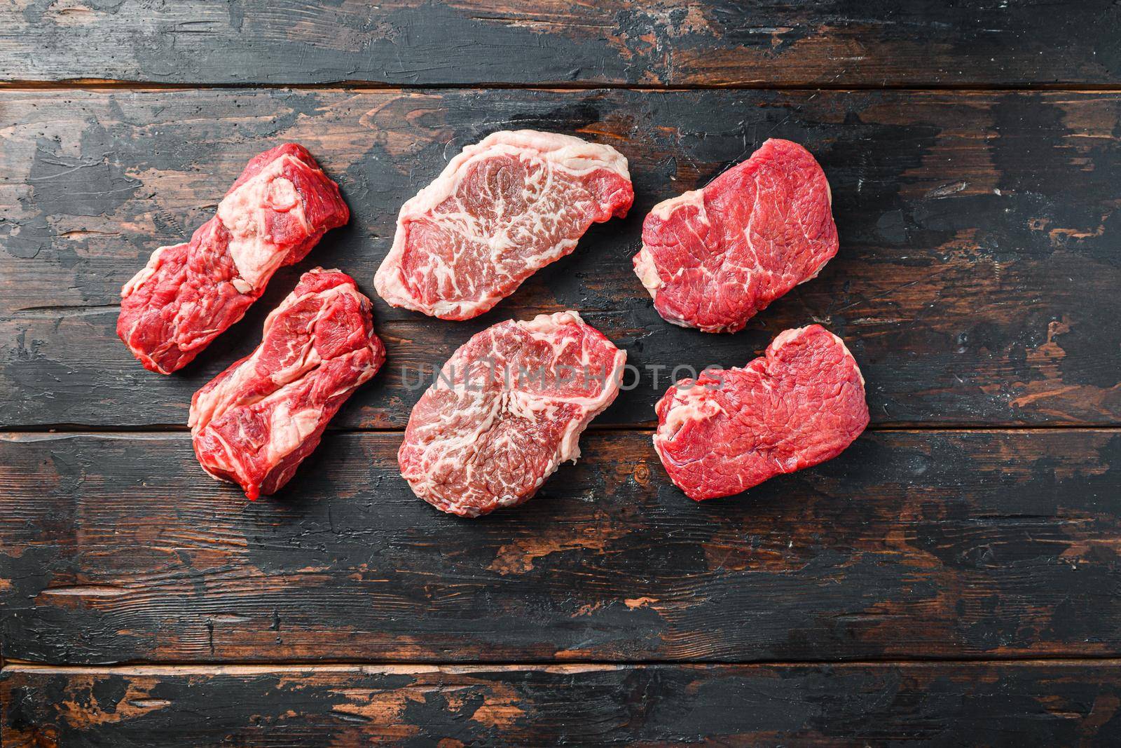 Variety of organic raw beef steakes rump, chuck roll and top blade cut on old rustic dark wooden background, top view with space for text