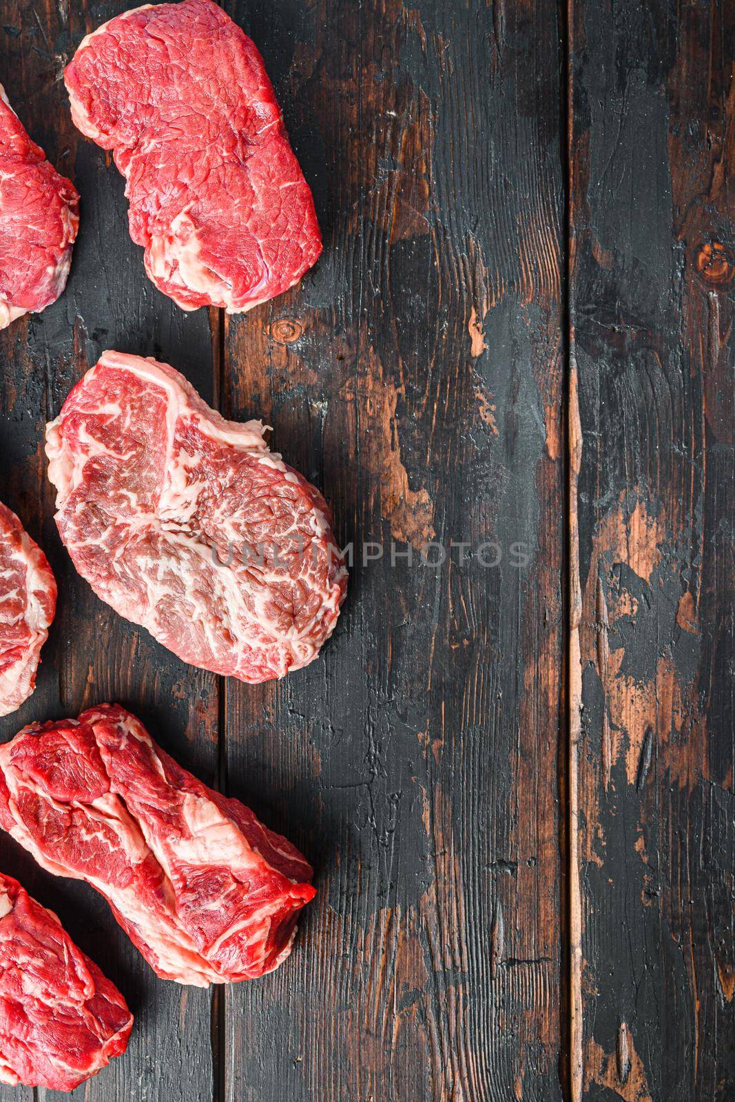 Variety of fresh Black Angus Prime raw beef steakes on old rustic dark wooden background, top view with space for text