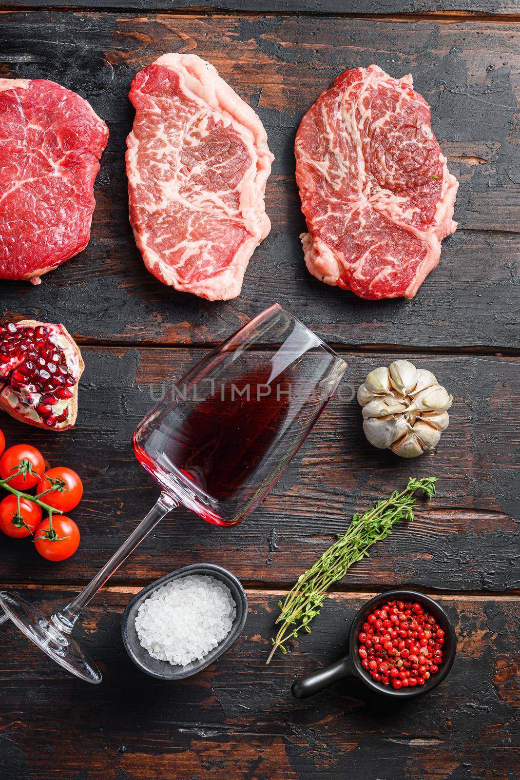 Set of different raw beef steaks with seasonings and red wine in bottle and glass on old wooden dark planks top view