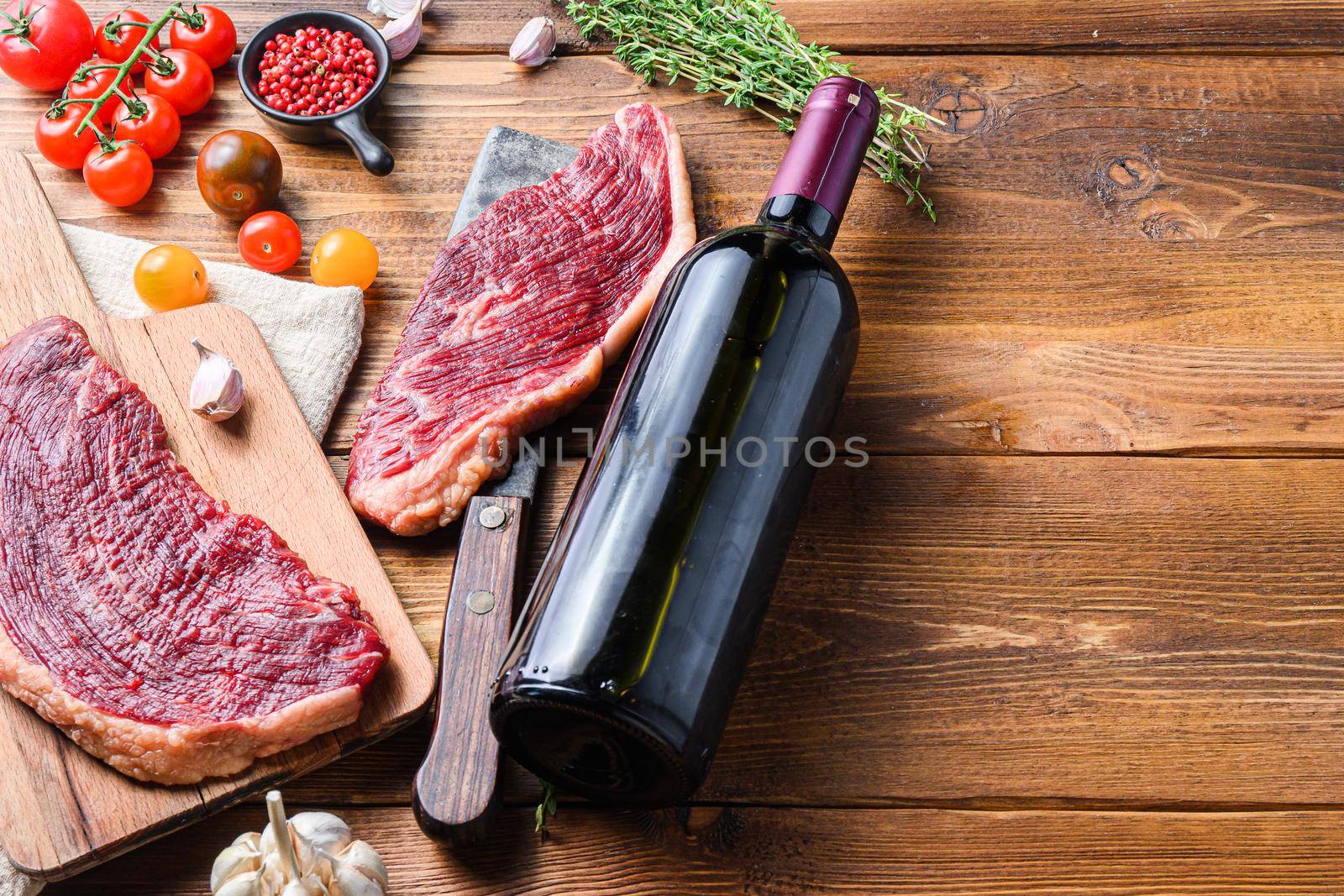 Picanha organic beef steaks over old american butcher cleaver with seasonings and red wine bottle on wooden table. Side view with space for text