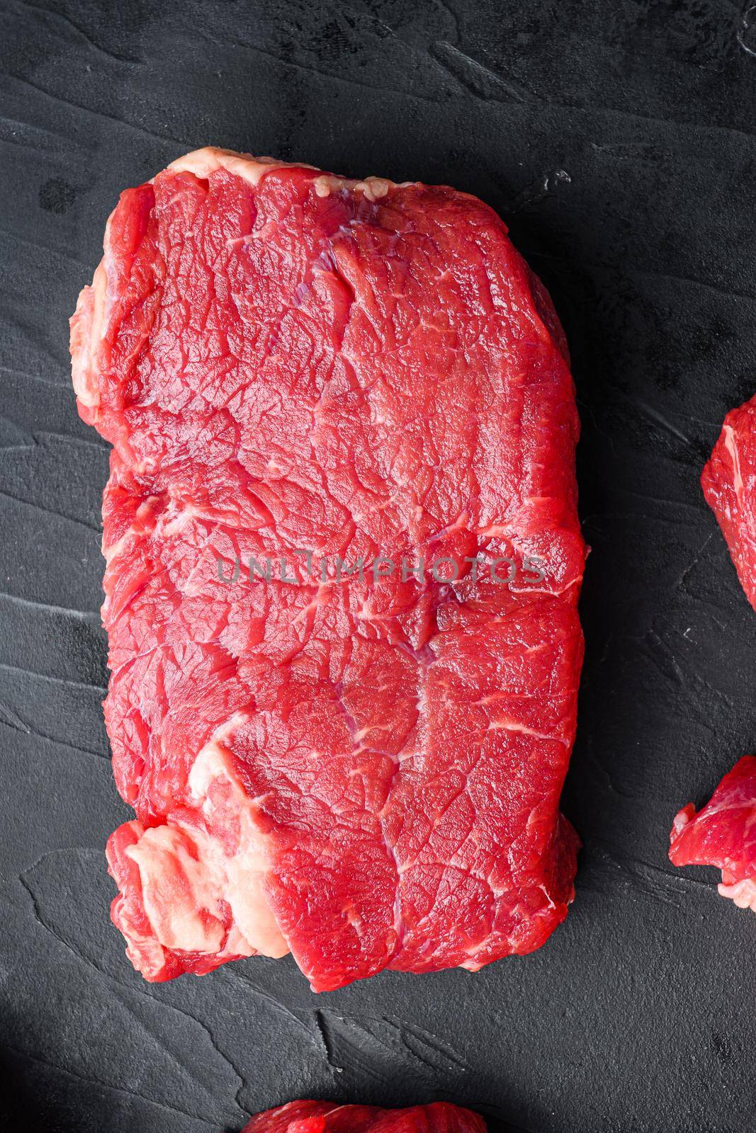 Organic rump beef steaks, top view on black textured table.
