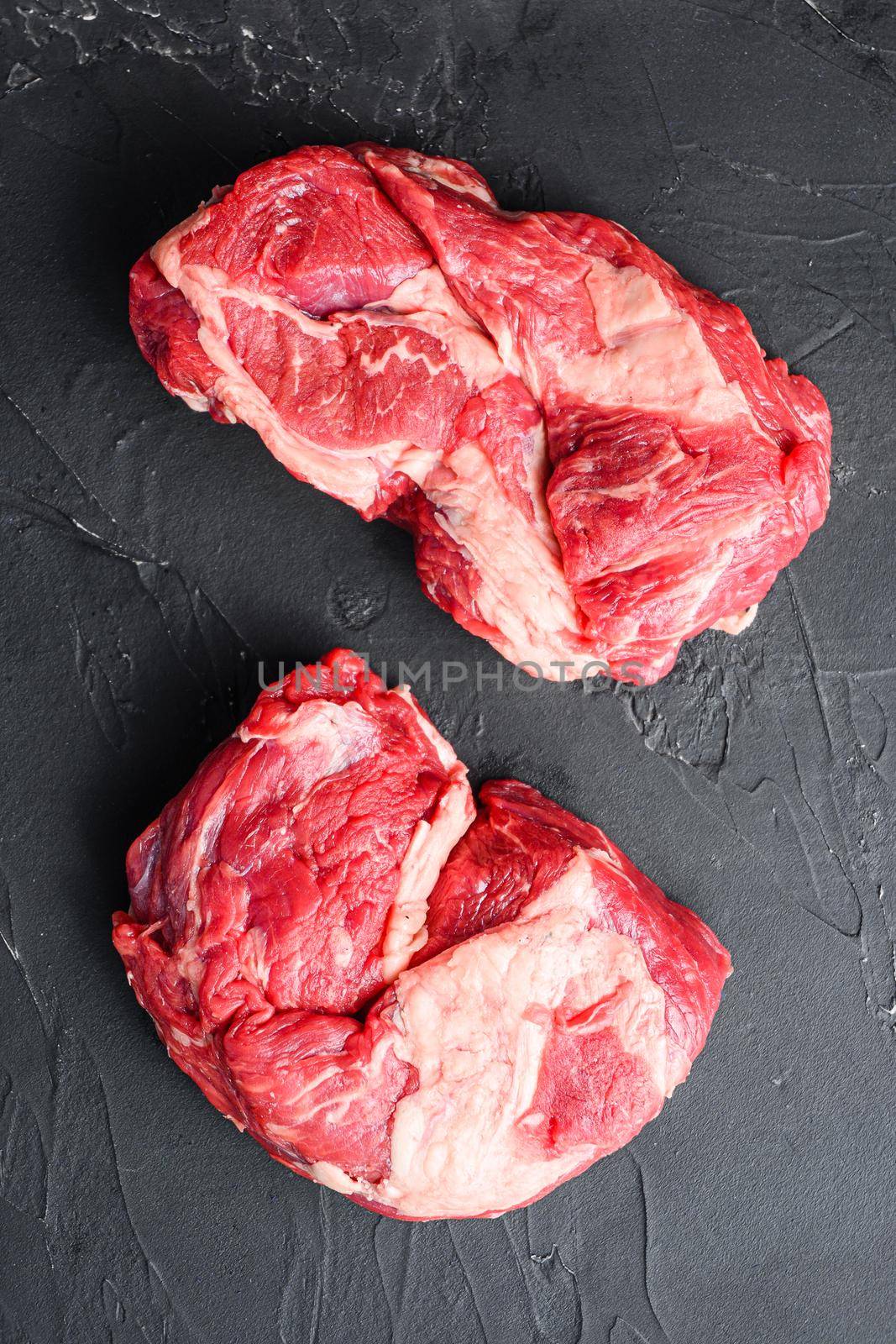 Raw chuck eye roll steak cuts, top view on black textured.