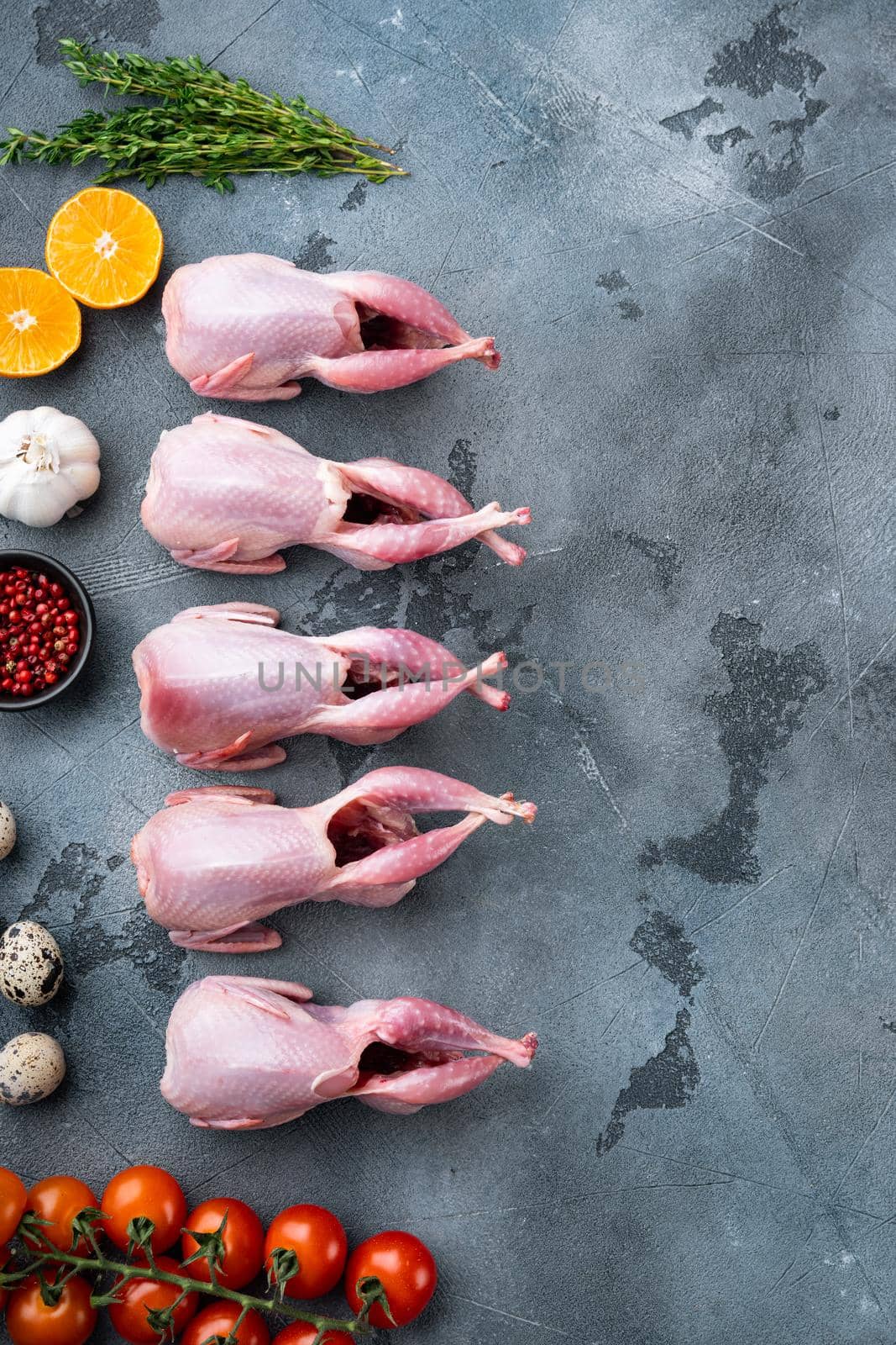 Whole quails meat with spices, herbs, vegetables, top view, on grey background with copy space
