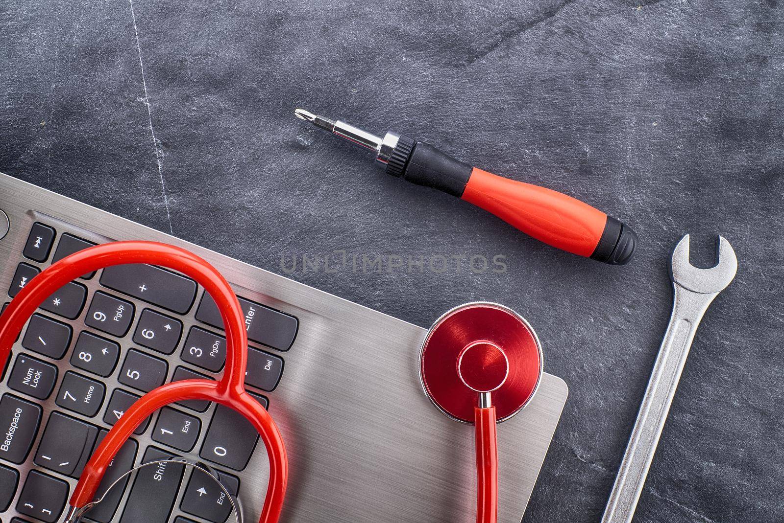 Computer repair or maintenance concept with a stethoscope to check the status or health of the device on top of a laptop with screwdriver and spanner