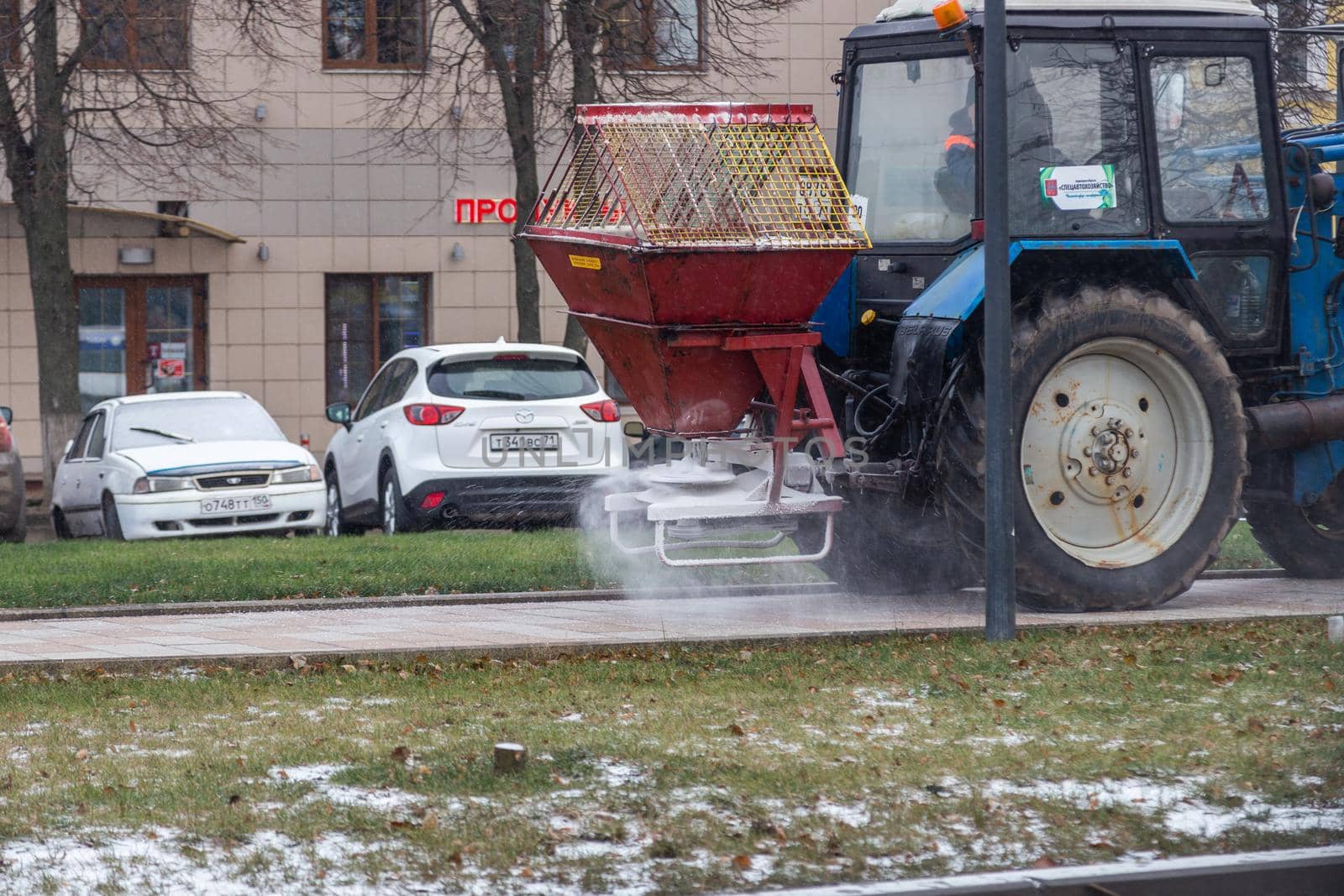 TULA, RUSSIA - NOVEMBER 21, 2020: Tractor spreading salt reagent over city pavement at winter daylight.