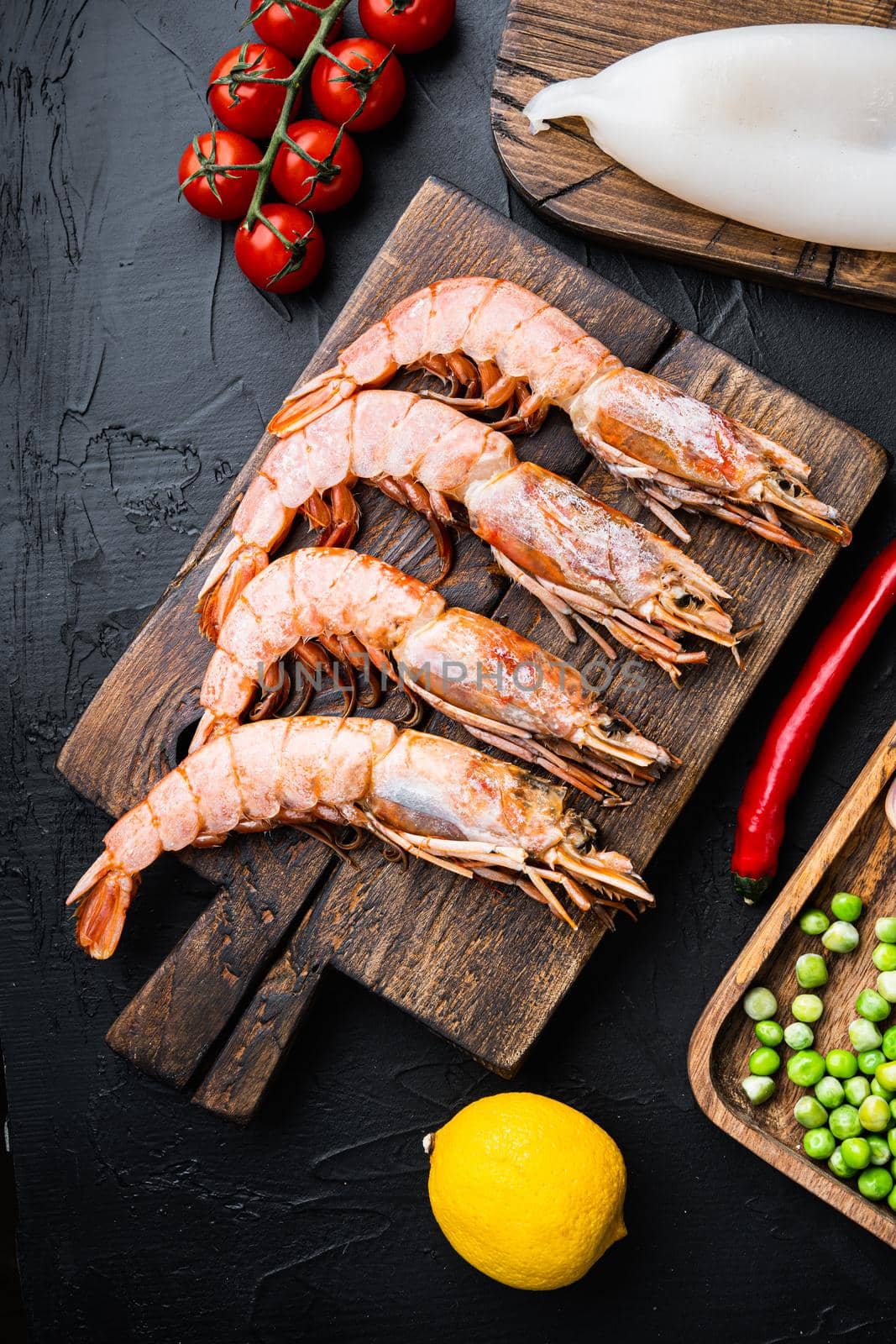 Set of king shrimps with ingredients for paella on black textured background, top view, food photo.