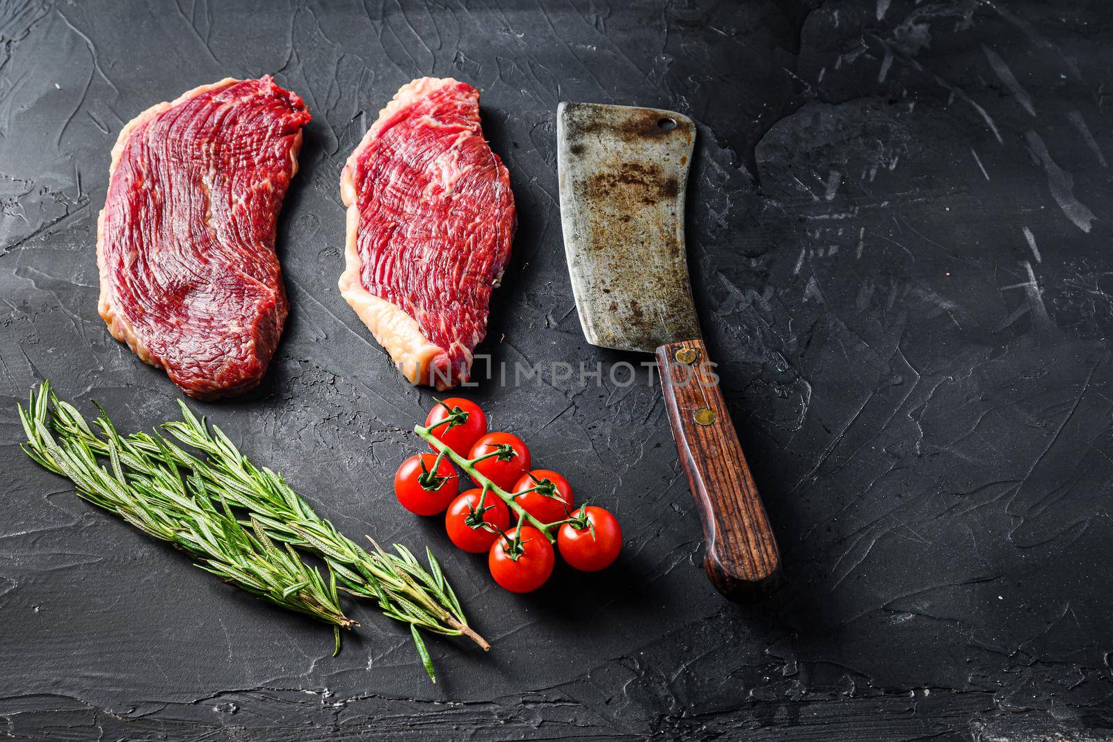 Picanha raw beef steaks with herbs and old butcher cleaver on black textured background, side view space for text