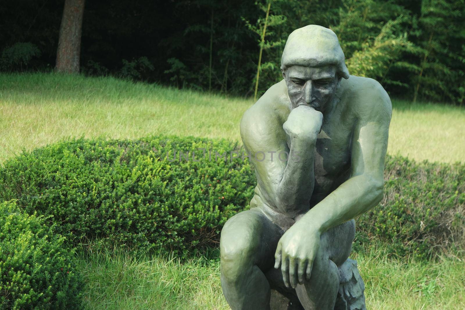 Green statue of thinker Auguste Rodin, setting naked on a rock by Photochowk