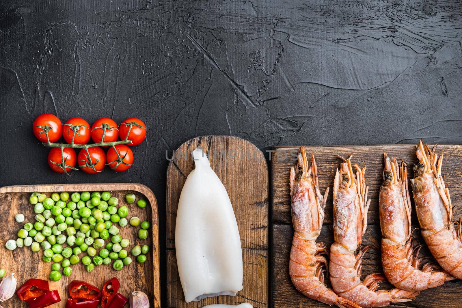 Traditional valenciana paella seafood ingredients with prawns, mussels, rice and spices on black concrete surface, flat lay with copy space, food photo.