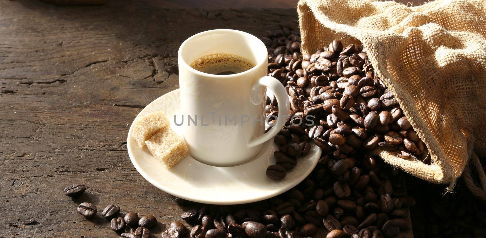 Hot cup of coffee espresso, coffee beans, canvas on old wooden table. Morning sun light. Copyspace for text