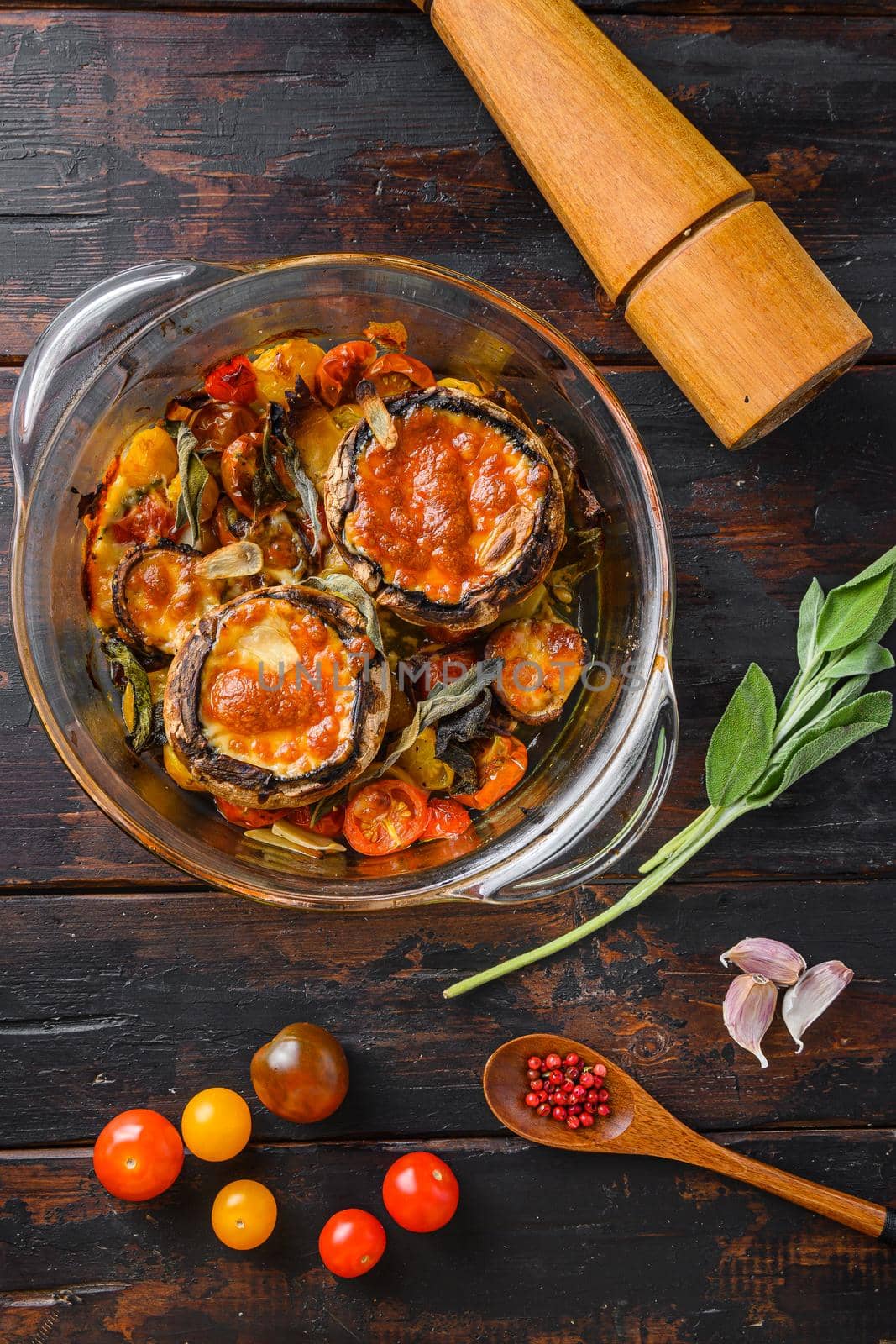 Portobello baked with cheddar cheese, cherry tomatoes and sage in glass pot on old wooden background top view