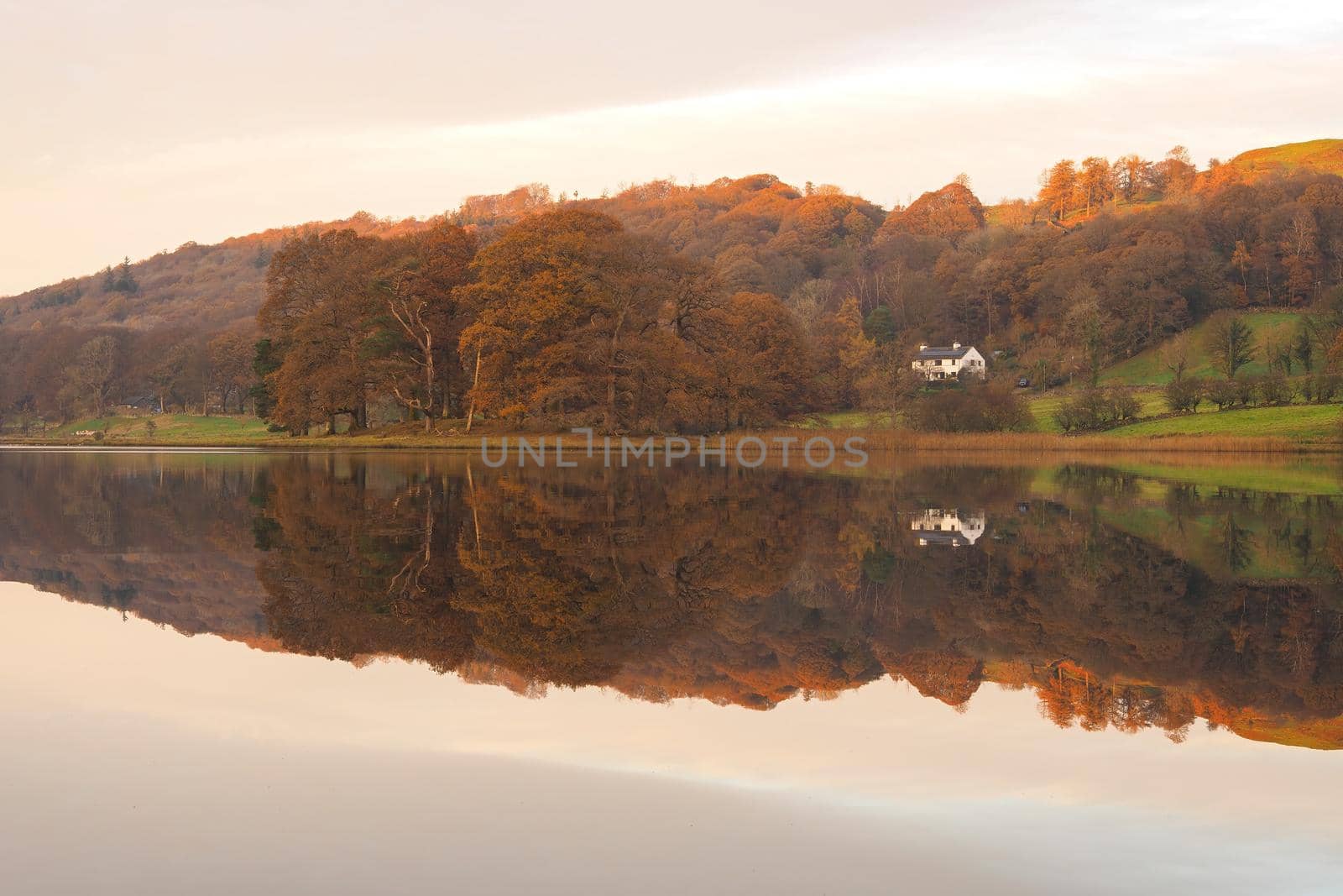 Peaceful dusk falls across Esthwaite Water with reflections in the water of buildings, trees and colourful clouds in a mackerel sky, Lake District, UK