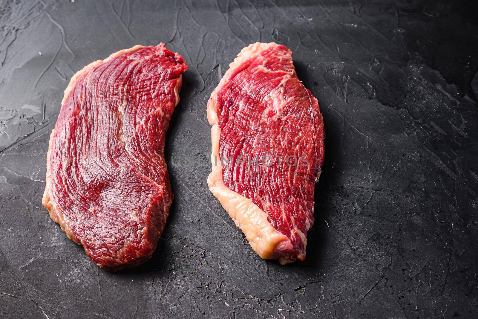 Organic raw picanha beef steaks, on black textured background, side view