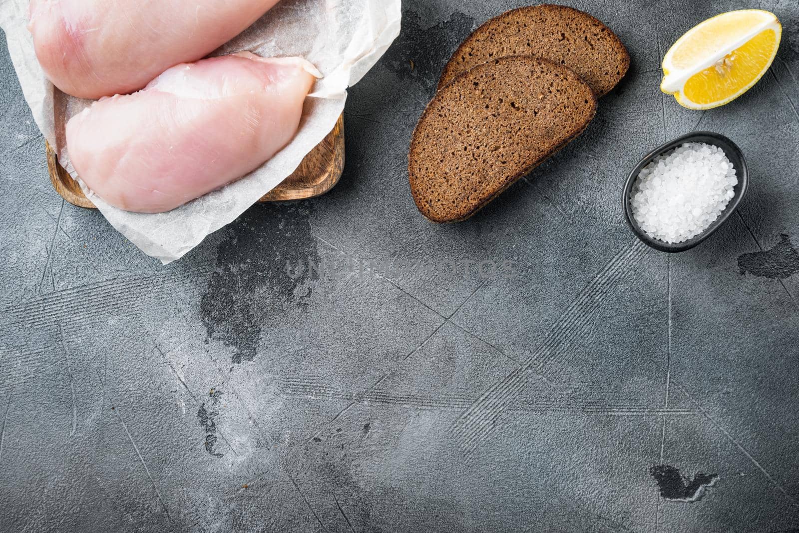 Raw crumbet chicken fillet with ingredient on grey background, flat lay with copy space