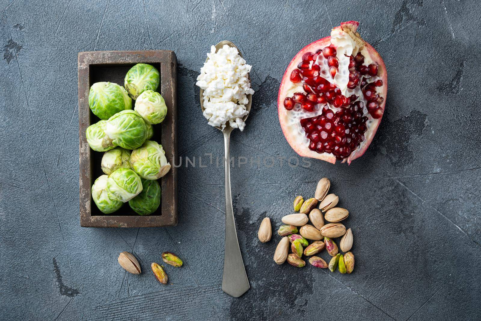Brussels sprouts with pomegranate, cottage cheese and pistachios, on grey background, flat lay