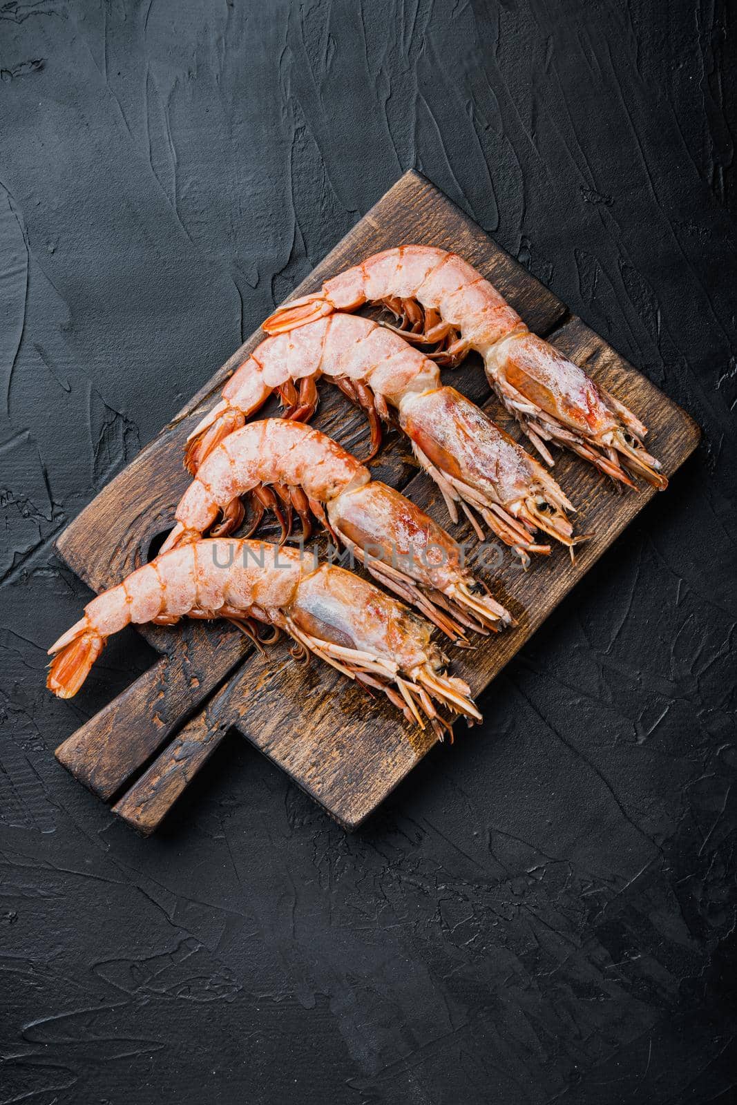 Fine selection of tiger prawns on cutting board on black textured background, top view, food photo.