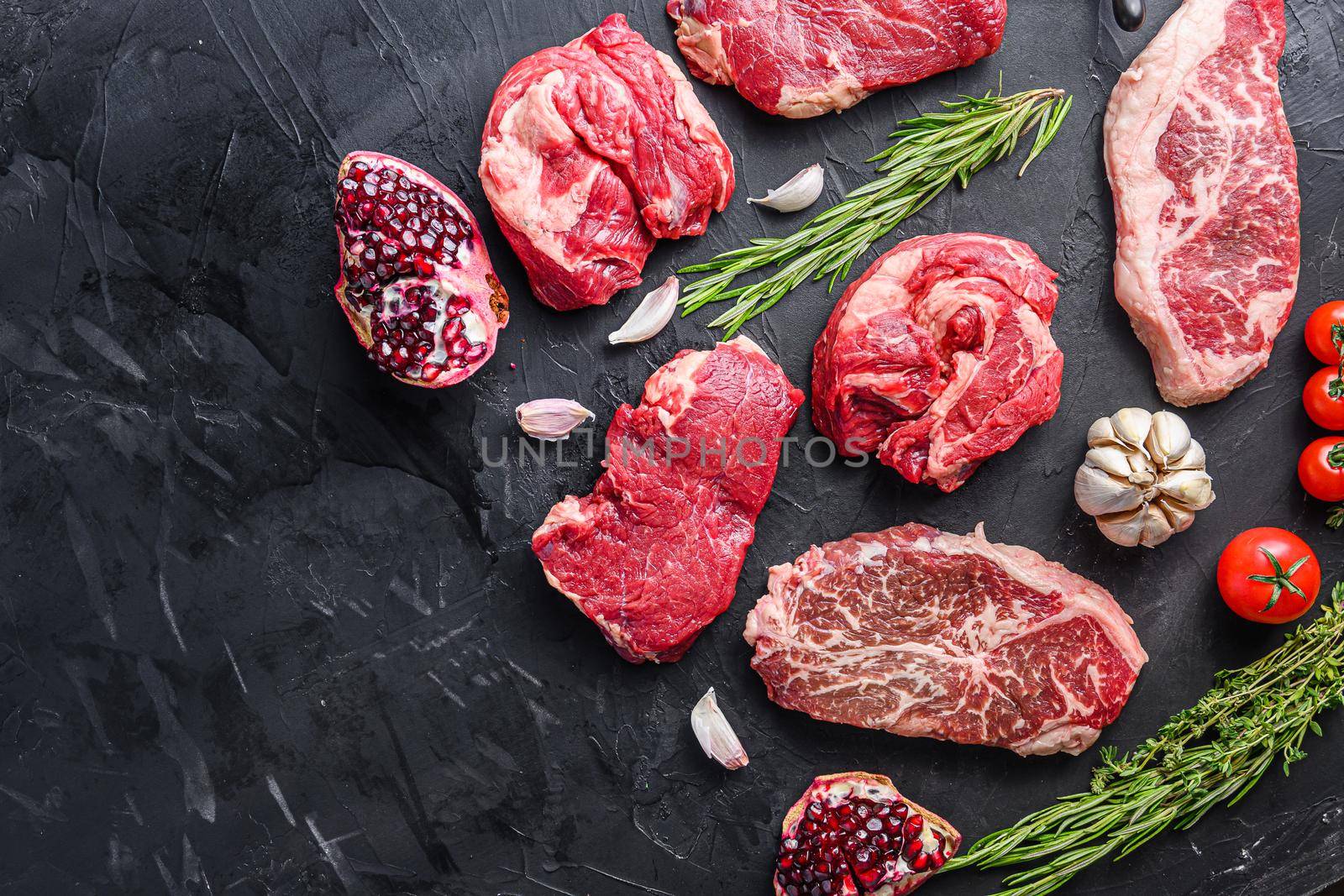 Alternative raw beef steak cuts with top blade, chuck roll and rump steak, with herbs and pomegranate top view, space for text
