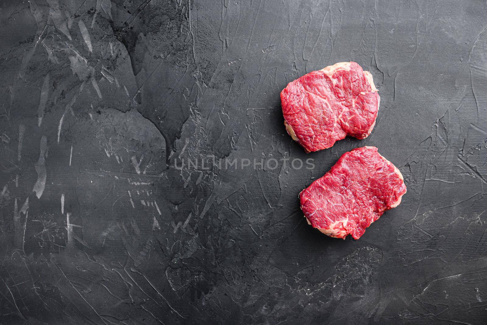 Raw rump steaks over black background, top view with space for text