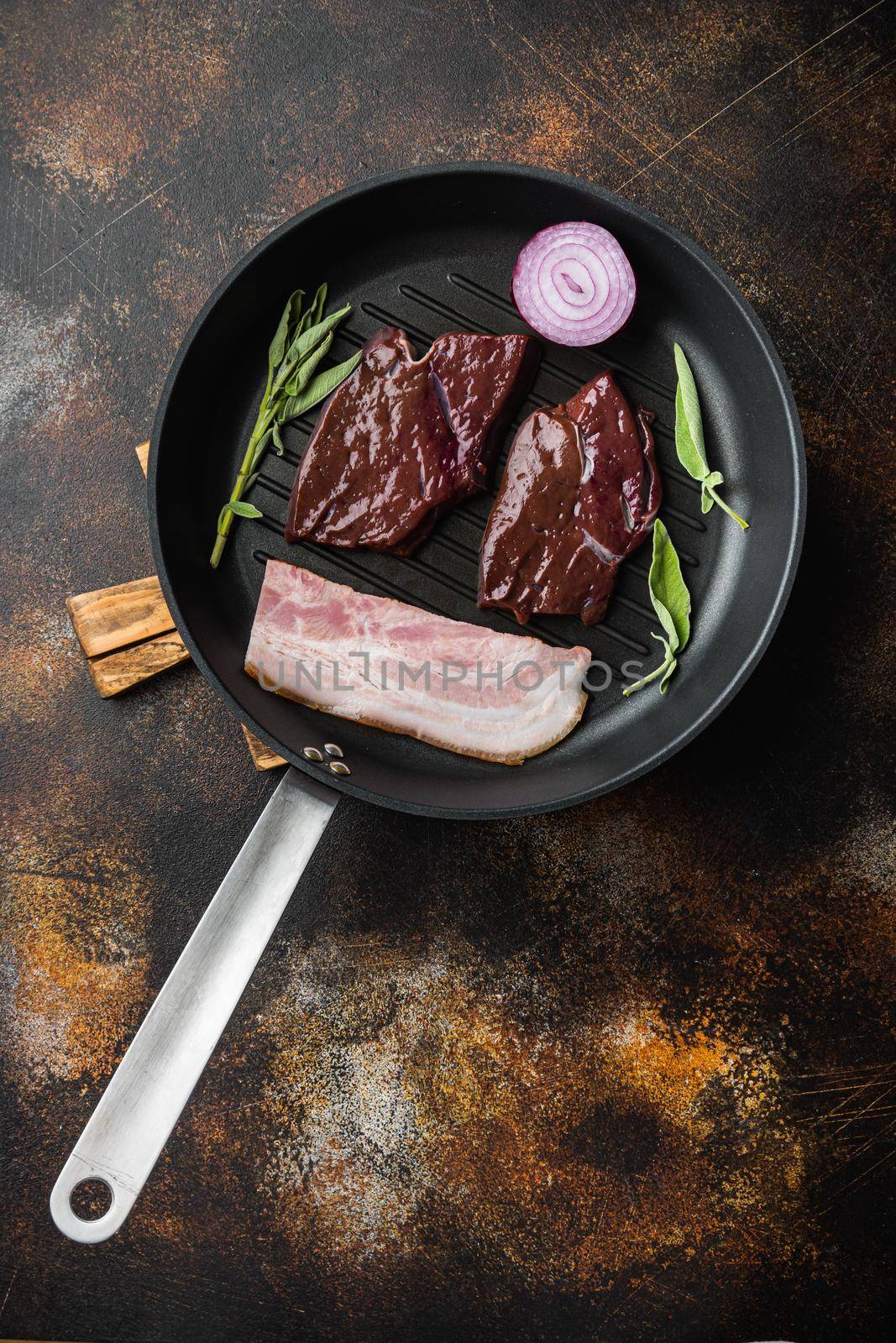 Beef liver sliced with bacon on grill pan over rustic background, top view.