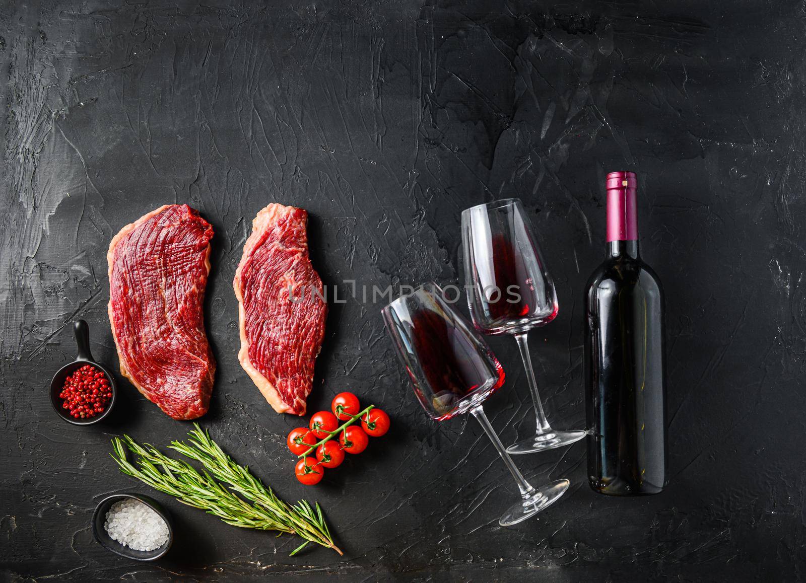 Raw picanha beef cuts with glasses of red wine, flat laym over black background space for text. Big size