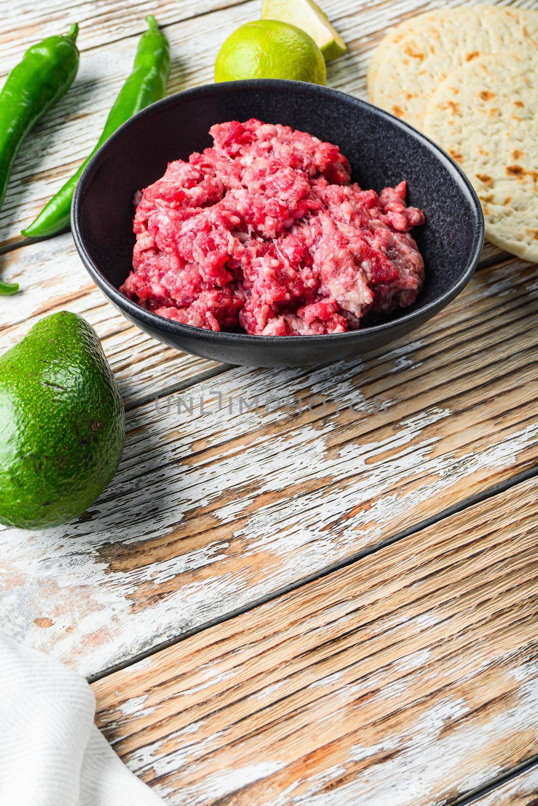 Mexican tacos with vegetables and minced meat ingredients over white textured wooden background , side view with space for text
