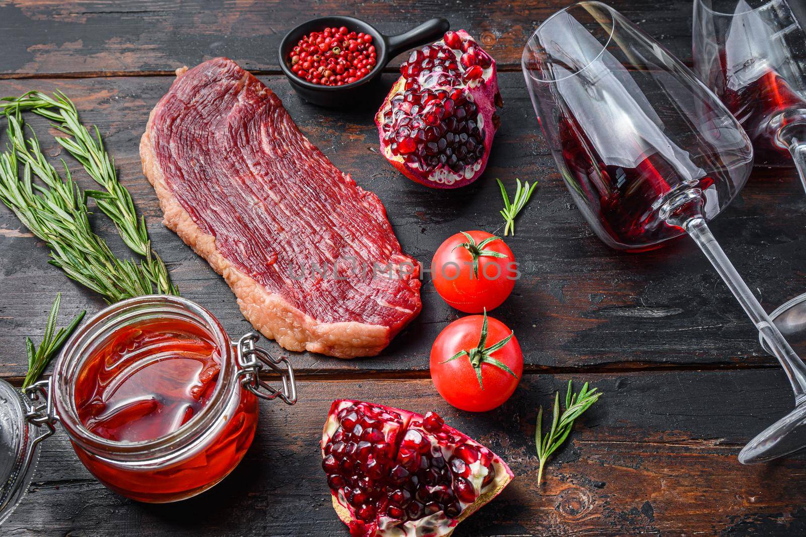 Raw picanha beef steak with rosemary, spicy chili oil, pomegranate and glass of red wine, on old dark wooden table side view, selective focus