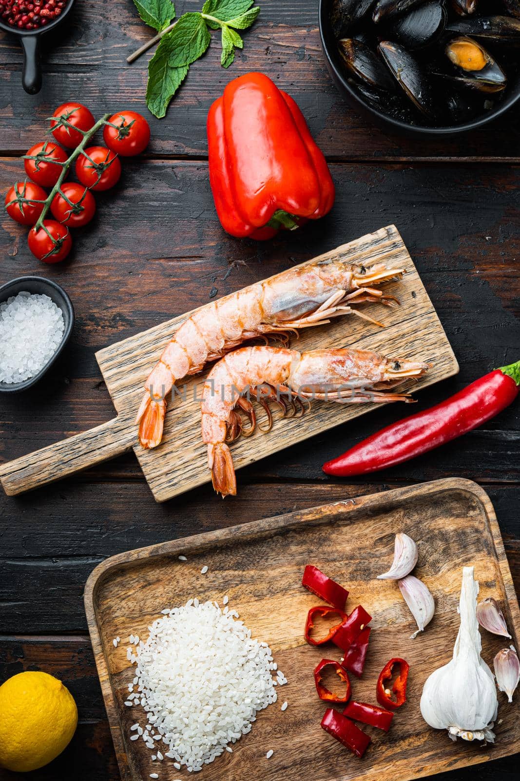 Traditional paella valenciana raw ingredients with shrimps, mussel, rice and squid over dark rustic wooden background, flat lay, food photo.