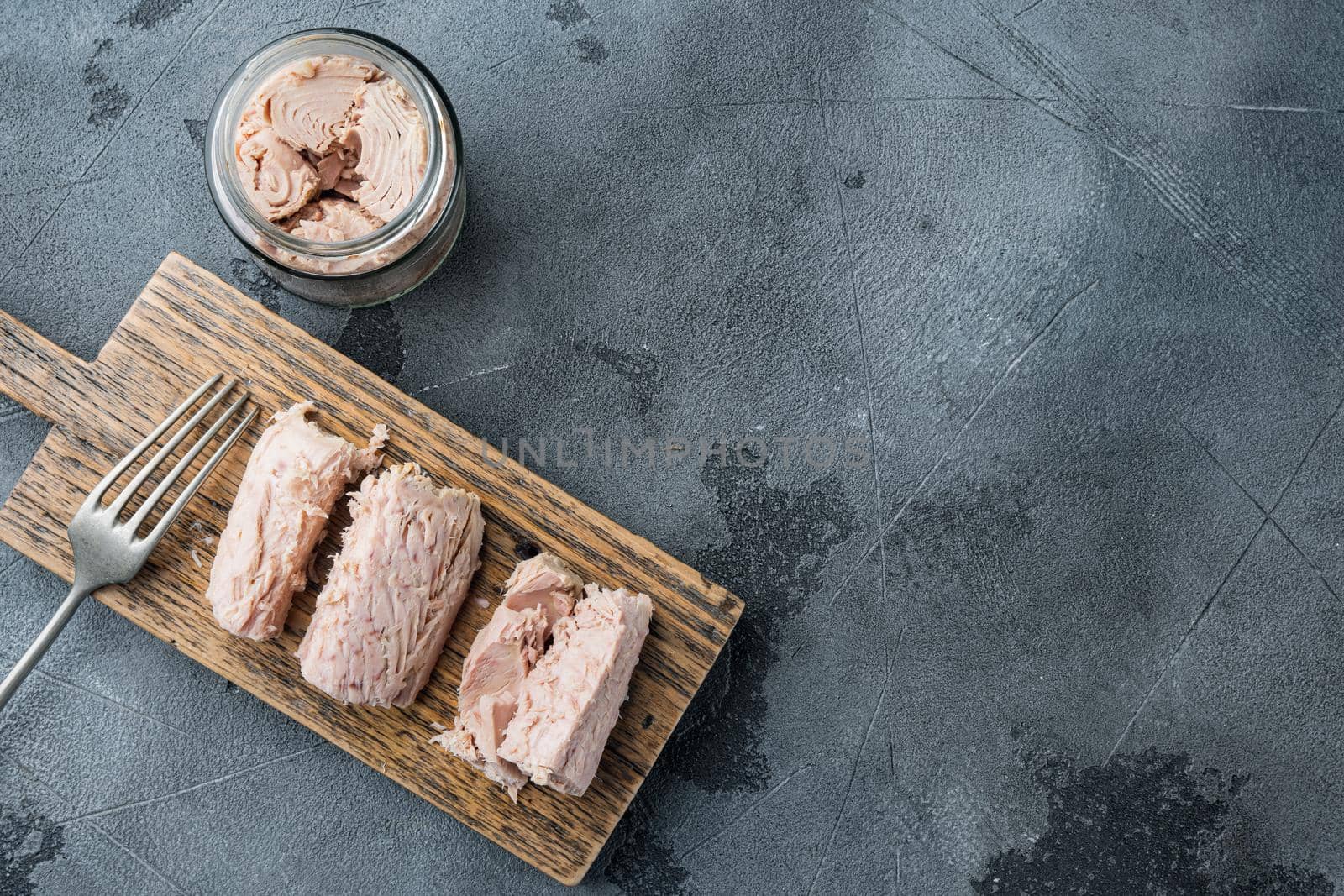 Canned tuna fillet meat in olive oil, on gray background, top view with copy space for text