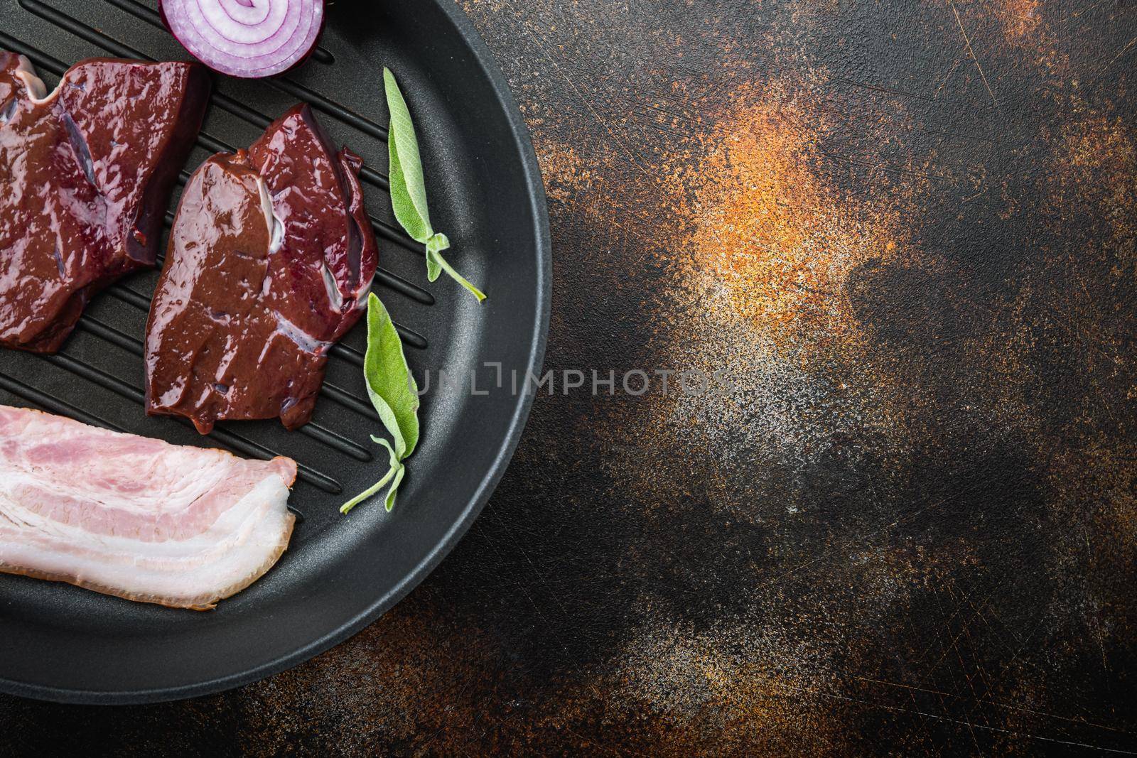 Beef liver sliced with bacon on grill pan over rustic background, top view with copy space.