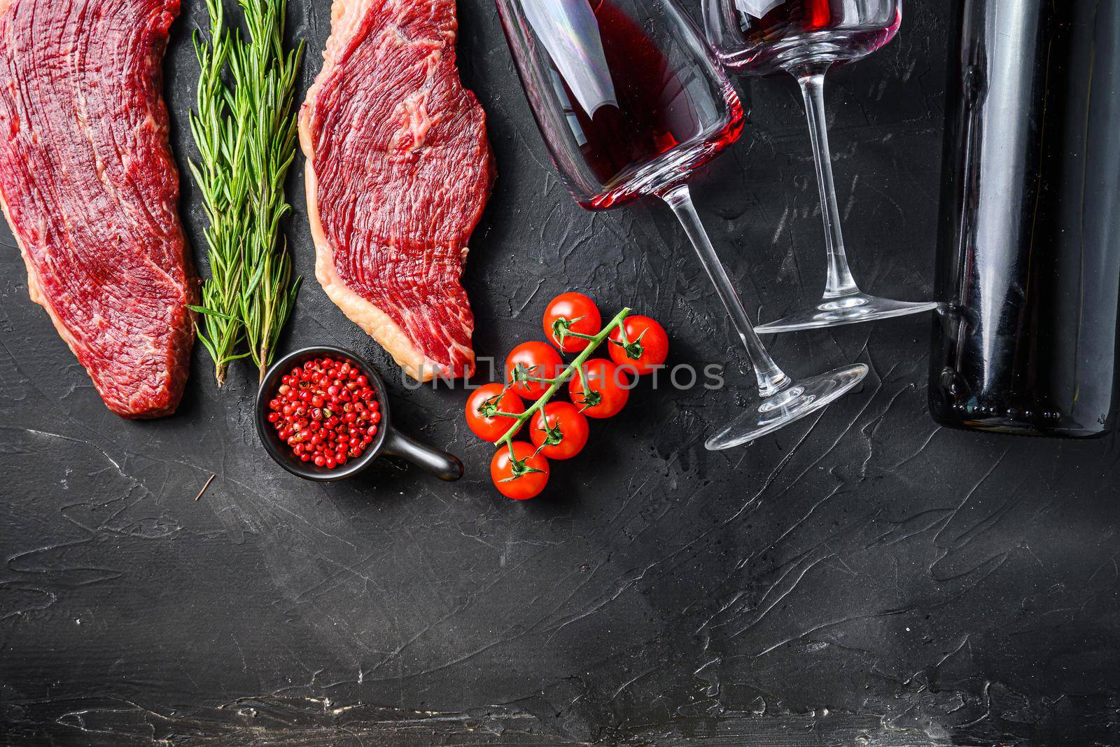 Raw picanha steaks near bottle and glass of red wine, over black textured table top view with space for text