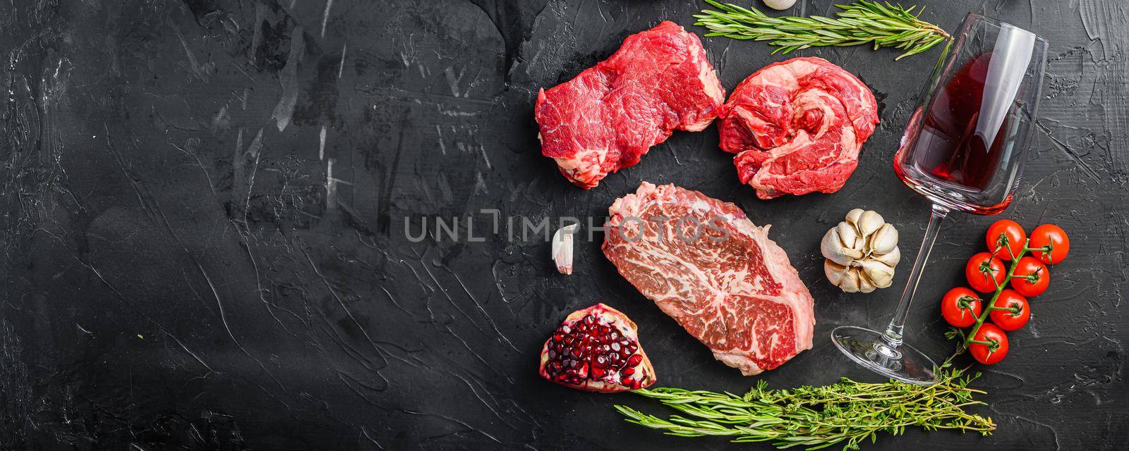 Set of various classic, alternative raw meat steaks with glasses of red wine over black background top view. Big size space for text banner
