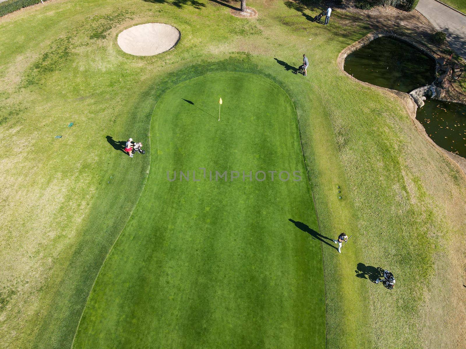 Aerial view of golf players around flag mark in hole on golf field by Bonandbon