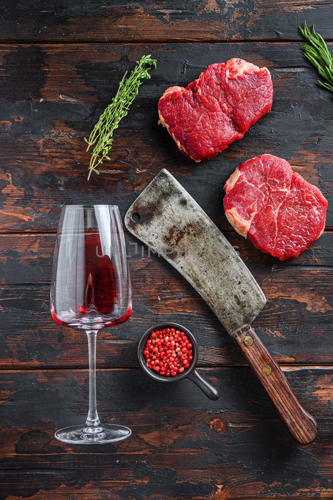Raw rump steaks with american butcher cleaver and two glass of red wine over dark old wooden background, top view