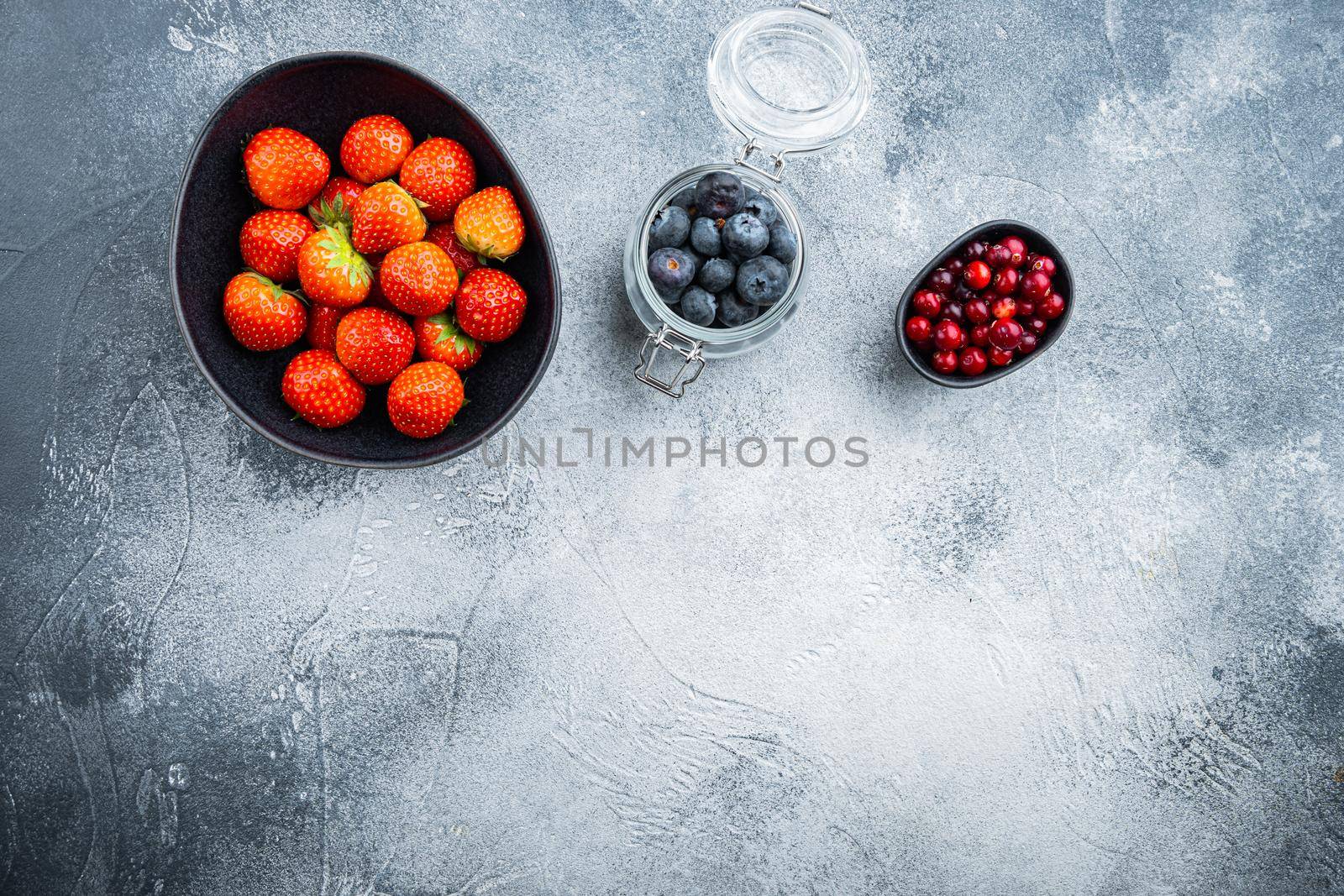 Ripe strawberry, cranberry and blueberry in bowl and jar, flat lay with space for text, on textured background.